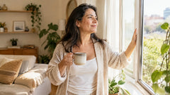 Mujer latina de unos 40 años abriendo la ventana de su sala por la mañana con una taza de té en la mano